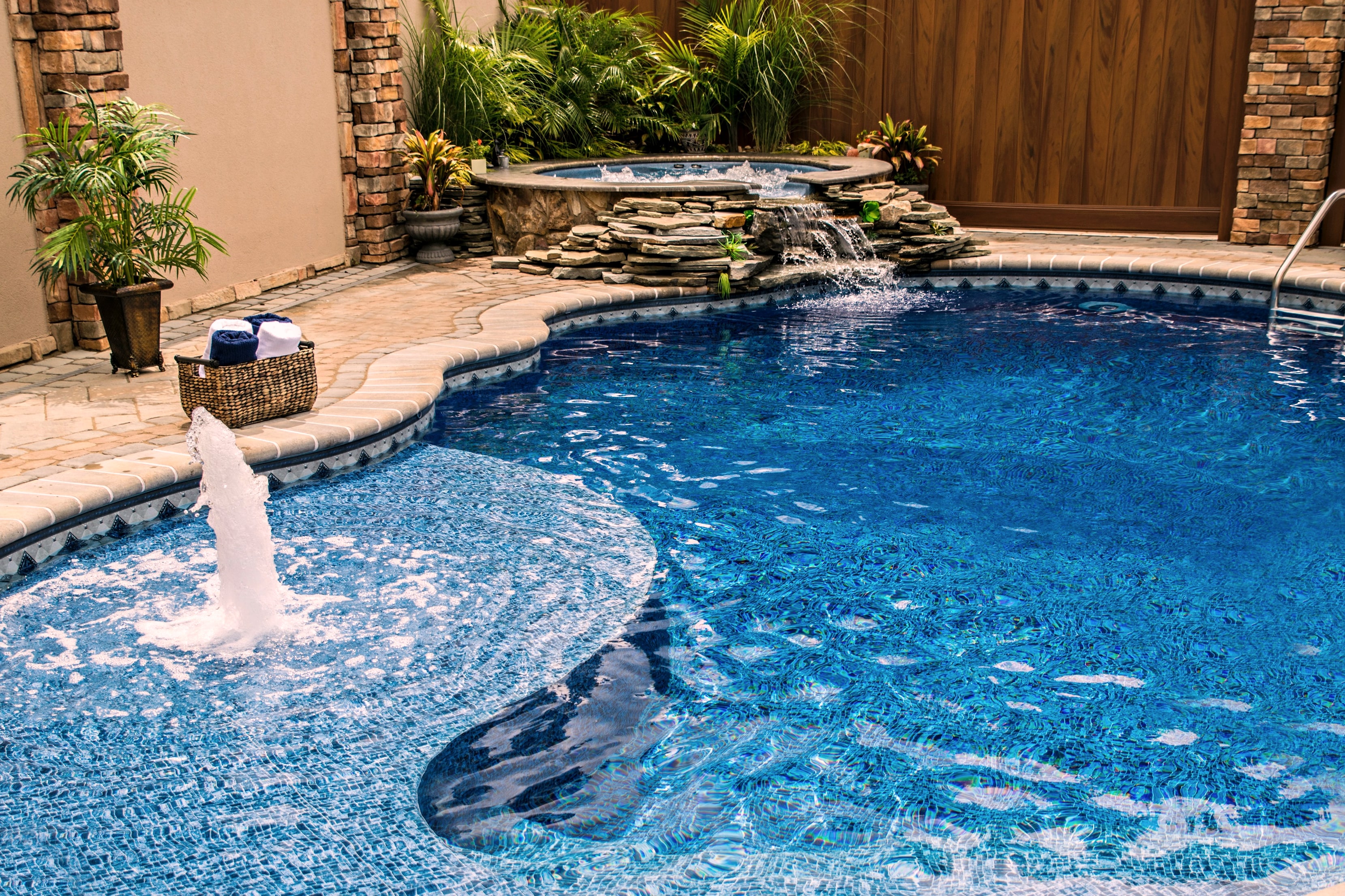 Curved inground pool with stone waterfall, raised spa and bubbler fountain