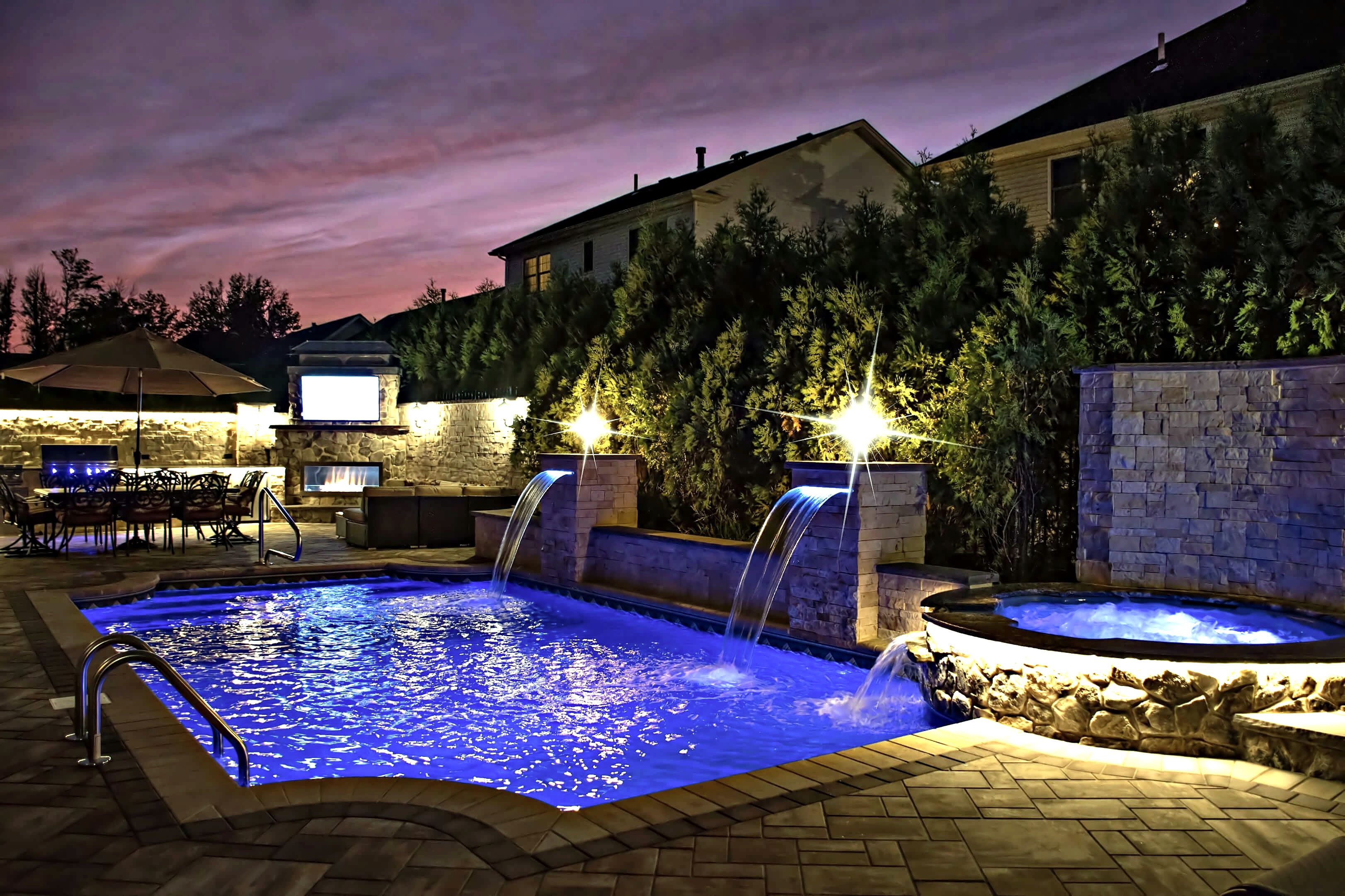 Dusk pool with lit waterfalls, spa, outdoor fireplace and dining area